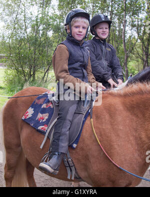 Selfoss, South Iceland, Iceland. 4th Aug, 2015. Two young siblings atop their steeds at the Fridheimar family run farm in Selfoss, South Iceland. Besides horticulture, the family offers visitors a horse show featuring the Icelandic horse breed brought by the first settlers from Scandinavia around 900 AD. Tourism is a growing sector of the economy with Iceland becoming a favorite tourist destination. © Arnold Drapkin/ZUMA Wire/Alamy Live News Stock Photo