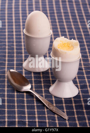 Egg cups with an eggs on top of a dark blue table cloth, with a spoon Stock Photo