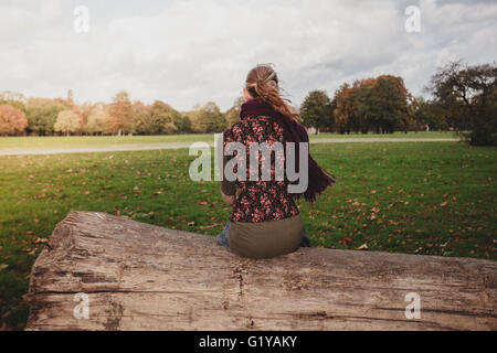 A young woman is sitting on a large fallen tree in the park on a sunny autumn day Stock Photo