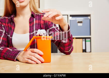 Woman throws paper into a small trash can on her desk Stock Photo