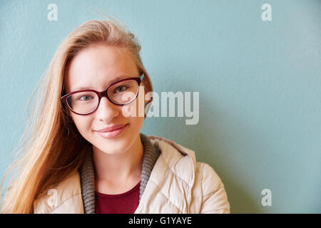 Young smiling woman wearing glasses stands in front of a light blue Stock Photo