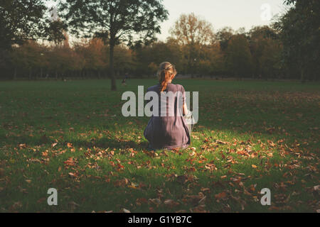 A young woman is siting on the grass in the park in the evening