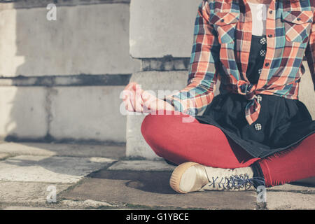 A young woman is sitting and meditating in the street Stock Photo