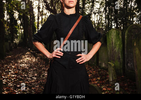 A young woman is walking amongst the tombstones in a cemetery Stock Photo