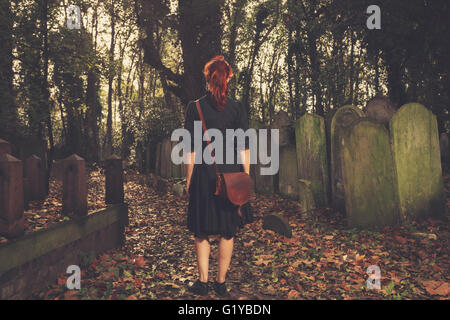 A young woman is walking amongst the tombstones in a cemetery Stock Photo