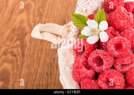 Delicious, fresh raspberries in a basket with a flower and leaves, on wooden table Stock Photo