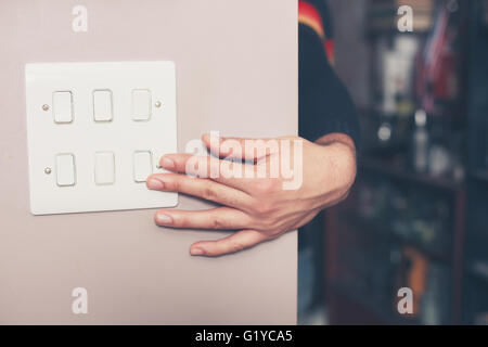 A young man's hand is switching on a light switch at home Stock Photo