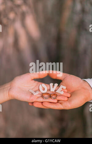 Golden wedding rings, wooden letters on the palms of bride and groom, close-up Stock Photo