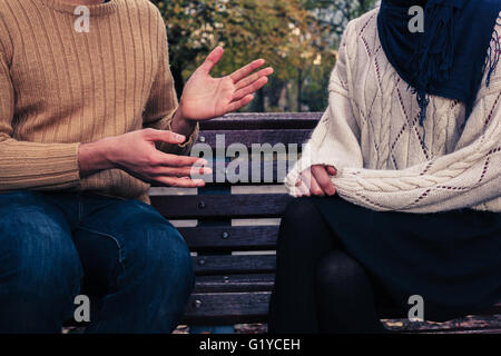 A young man and woman are sitting on a park bench and arguing Stock Photo