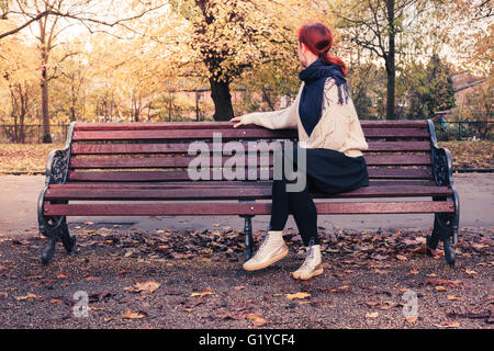A young woman is sitting on a park bench on a sunny day in autumn Stock Photo
