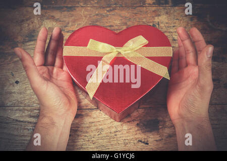 A man's hands are resting on a wooden surface with a heart shaped box Stock Photo