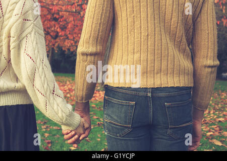 A young couple is holding hands in the park by a tree in autumn Stock Photo