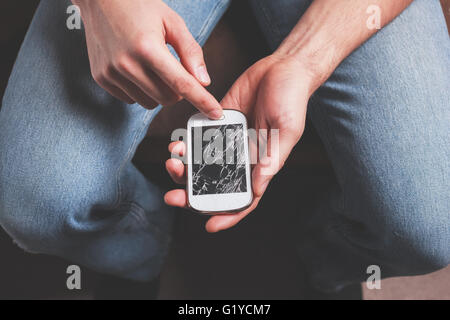 A young man is sitting holding a broken smart phone Stock Photo