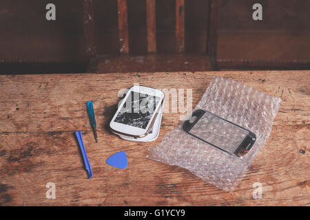 A broken smart phone and the tools required to fix it Stock Photo