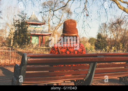 A woman wearing a winter hat is sitting on a park bench near a pagoda Stock Photo