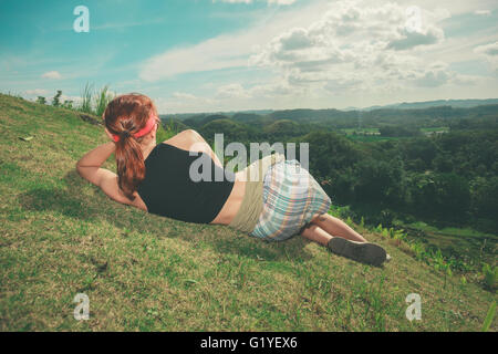 A young woman is lying on the hillside and is admiring the view of the chocolate hills in Bohol, Philippines Stock Photo