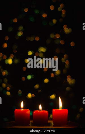 Three red candles burning with colourful lights defocused Stock Photo