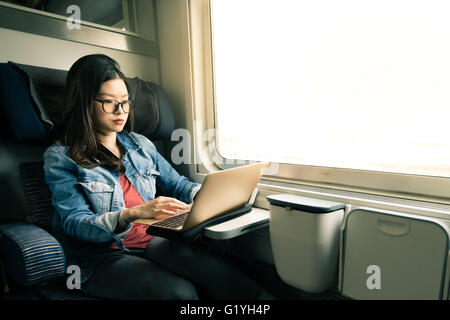 Asian woman work on laptop on train, business travel concept, warm light tone