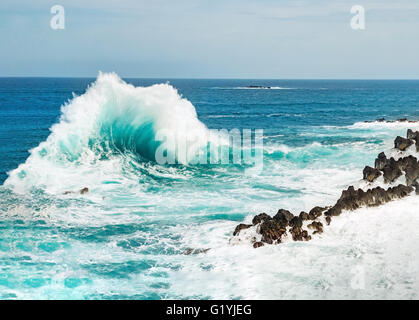 Ocean wave splashing sea water on rocky shore line, with water foam and blue sea water on the background rough seas. Porto Moniz Stock Photo