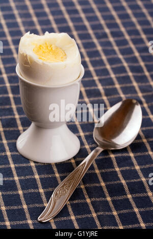 Egg cup with an egg on top of a dark blue table cloth, with spoon Stock Photo