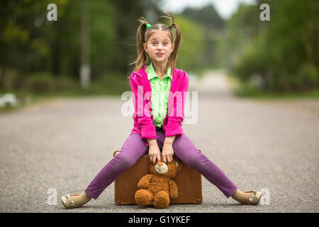 Little traveller girl on the road with a suitcase and a Teddy bear. Stock Photo