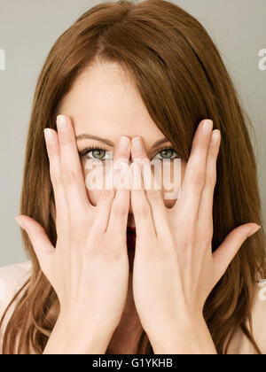 Portrait of a Woman Covering Her Face With Her Hands And Peeking or Peering Though Her Open Fingers Looking at the Camera Stock Photo