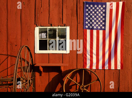 Close up US flag on a red barn and rusty wheels, New Jersey farm, USA, US flag rural America historical images colonial US flag close up spring summer Stock Photo
