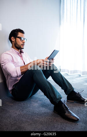Serious businessman using tablet computer while sitting on the floor Stock Photo