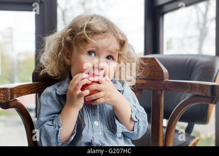 little child eating red apple indoors Stock Photo