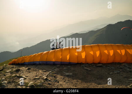 A paraglider starts catching the wind in its wings as the flyers are caught in a silhouette in Bir Billing, Himachal Pradesh, Ind Stock Photo