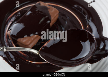 Closeup of cookie and silver spoon covered in dark melted chocolate on white plate Stock Photo