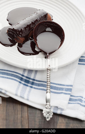 Sweet tube covered in dark melted chocolate with vintage silver spoon on white plate Stock Photo