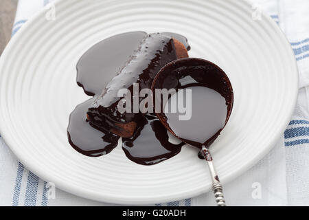 Closeup of sweet tube covered in dark melted chocolate with vintage silver spoon on white plate Stock Photo