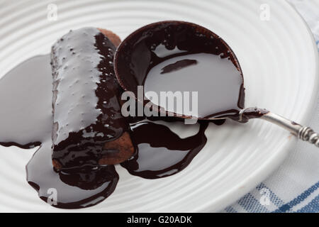 Closeup of sweet tube covered in dark melted chocolate with vintage silver spoon on white plate Stock Photo