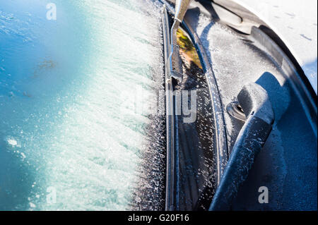 Car windshield and wipers covered in frost in winter, partially shaded. Stock Photo