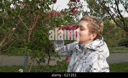 Pretty blond girl sniffing lilac flowers in park Stock Photo