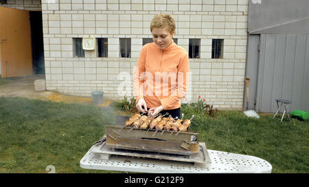 Girl cooks barbeque skewers with meat on brazier Stock Photo