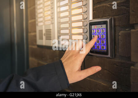 Woman dialing pass code on intercom security keypad to open entrance door of the apartment building. Stock Photo