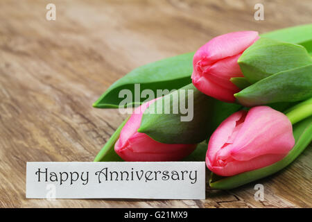 Happy Anniversary card with three pink tulips on wooden surface Stock Photo