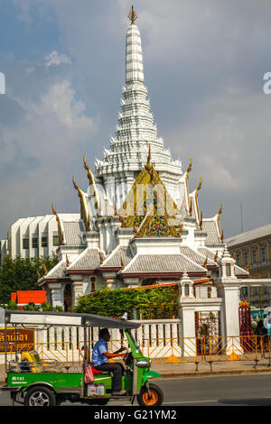 A man driving a modified tuk-tuk is photographed in a background of the Bangkok city pillar shrine (Lak Mueang) in Bangkok, Thailand. Stock Photo