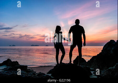 Silhouette young couple standing on the beach holding hands and watching  the tropical sunset Stock Photo