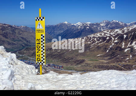 Yellow danger warning sign by snowy cliff edge, Andorra, Pyrenees Stock Photo