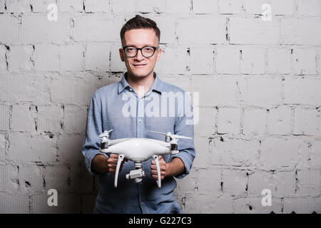 Young stylish Man in glasses holding the quadcopter drone DJI Phantom 4 on a grey brick wall Stock Photo