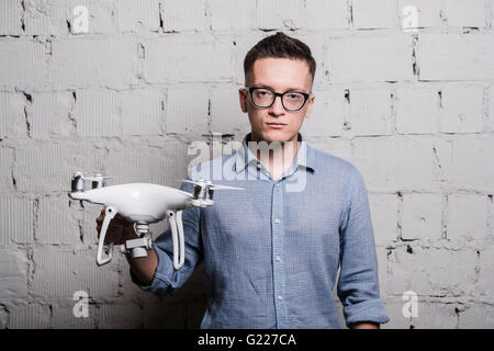 Young stylish Man in glasses holding the quadcopter drone DJI Phantom 4 on a grey brick wall Stock Photo