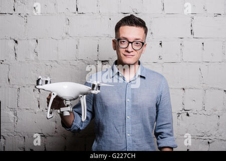 Young stylish Man in glasses with quadcopter drone on a grey brick wall Stock Photo