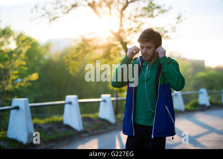 Toned Photo of Common young lonely man walking in the city listening to music with in-ear headphones at sunset. Soft warm light. Stock Photo