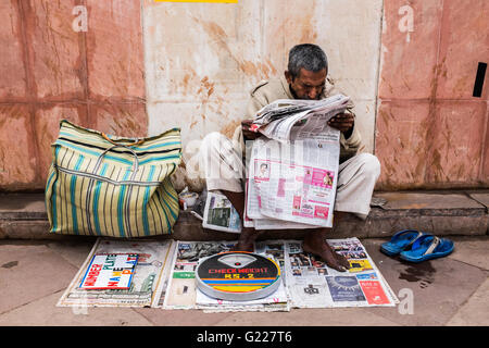 Man reading paper whilst he waits for customers to weigh themselves, Delhi, India Stock Photo