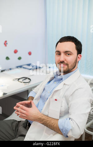 Calm doctor or consultant sitting at desk with his stethoscope on  table looking to the camera Stock Photo