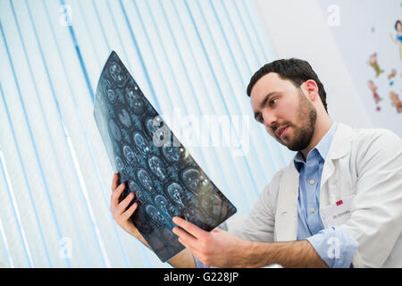 Closeup portrait of intellectual man healthcare personnel with white labcoat, looking at brain x-ray radiographic image, ct scan, mri, clinic office background. Radiology department Stock Photo