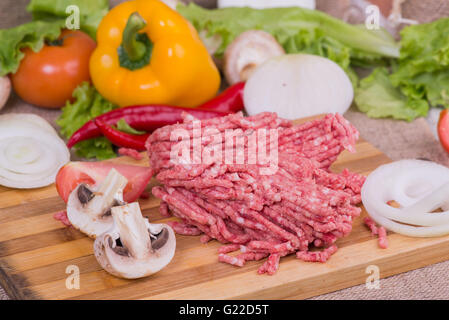 Raw minced pork in a plate and fresh vegetables on table close-up. top view Stock Photo